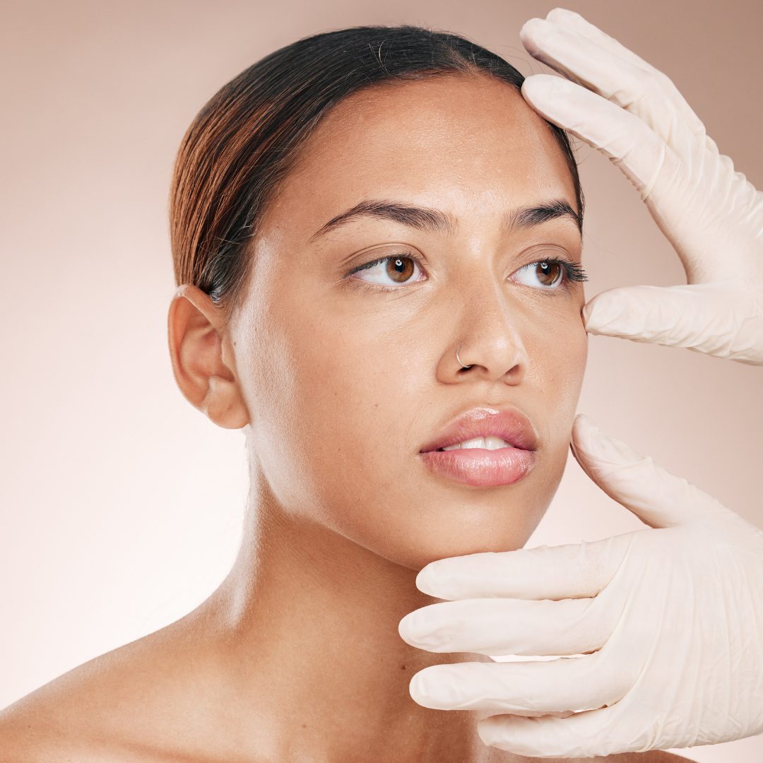 Woman with medium skin tone being examined by a professional wearing white gloves, focusing on her facial skin.